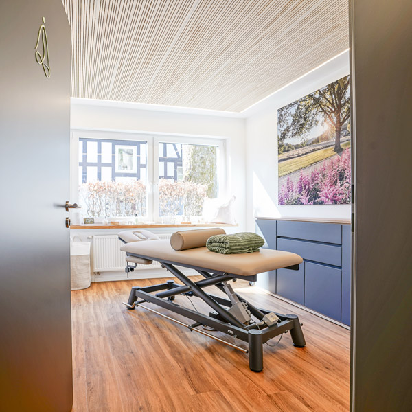 Offene Tür zum Behandlungsraum mit Massageliege und gemütlicher Einrichtung